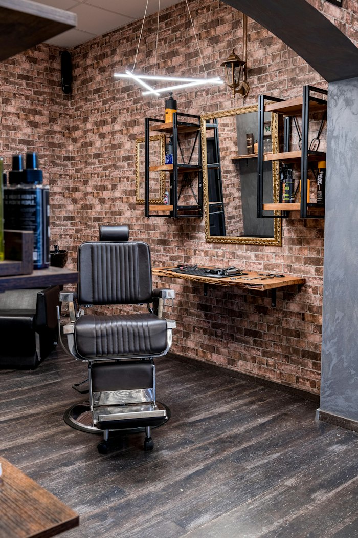 A black leather barber chair beside a live-edge oak shelf on a wide-plank floor
